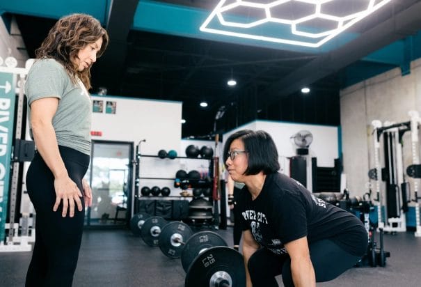girl in black shirt lift weight with personal trainer